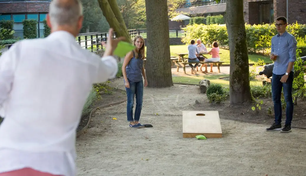 Mensen spelen cornhole in de tuin met houten bord en cornhole zakjes.